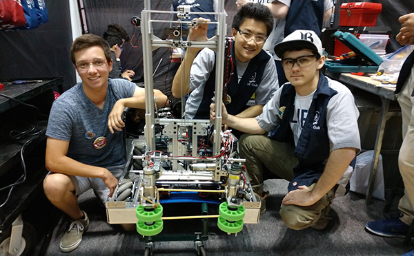 Male students squatting by robot